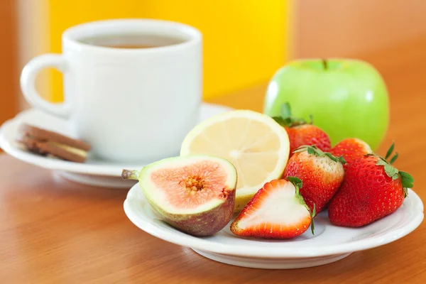 Tasse de thé, biscuit, pomme, citron, figue et fraises sur une assiette — Photo