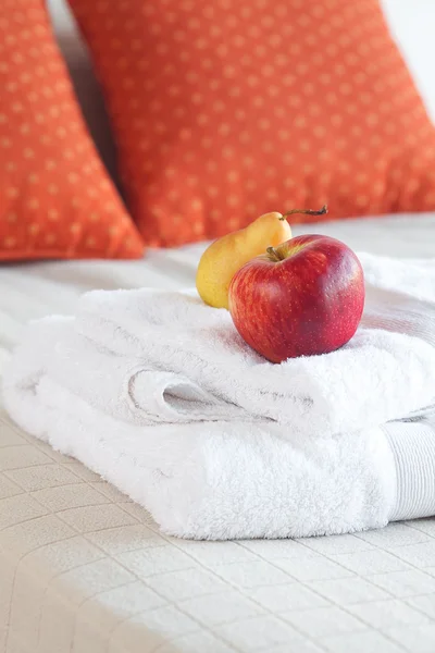Яблоко и груша на полотенцах на кровати с двумя подушками — стоковое фото