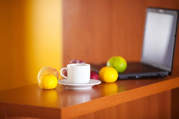 Laptop, cup och frukter på skrivbordet — Stockfoto