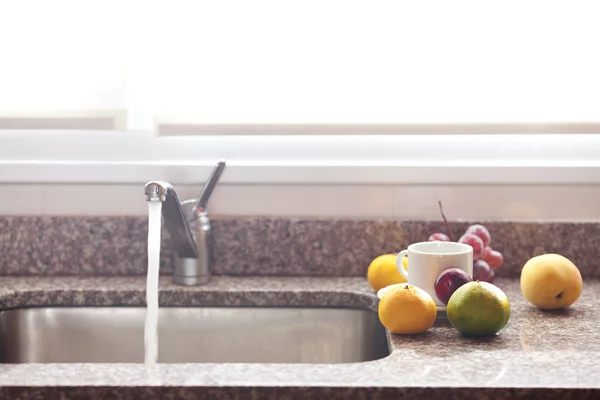 Cup, fruits and faucet on the kitchen — Stock Photo, Image