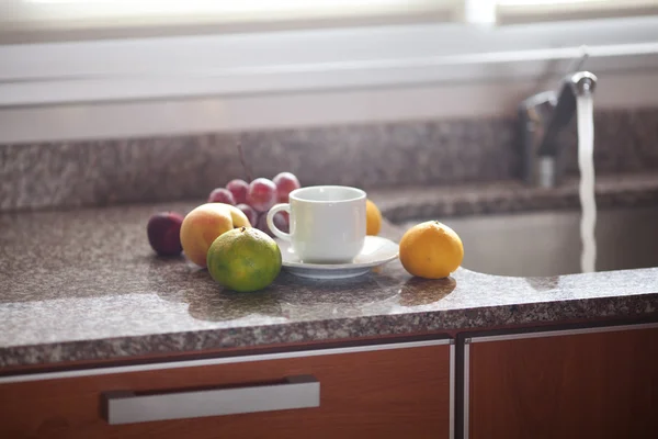 Xícara, frutas e torneira na cozinha — Fotografia de Stock
