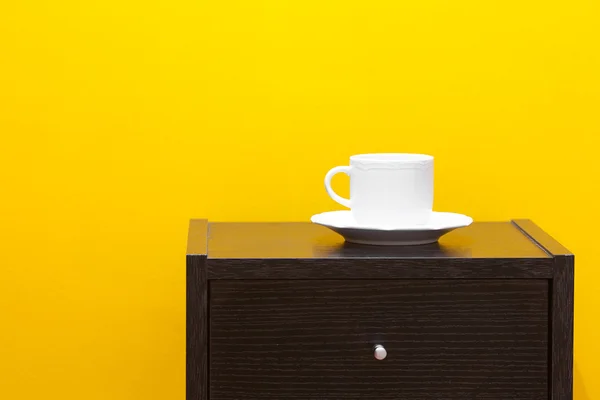 Mesa de cabeceira e xícara contra uma parede amarela no apartamento — Fotografia de Stock