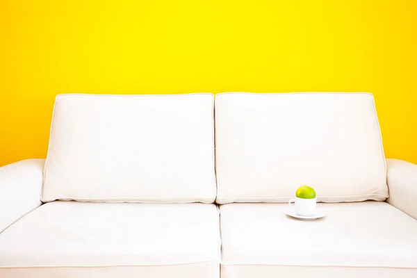 Biała kanapa i kubek z mandarynki przeciwko żółte ściany — Zdjęcie stockowe