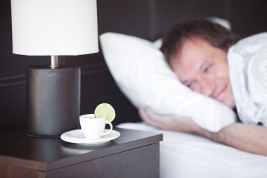 Man sleeping on a bed, a cup of tea on the bedside table and lam clipart