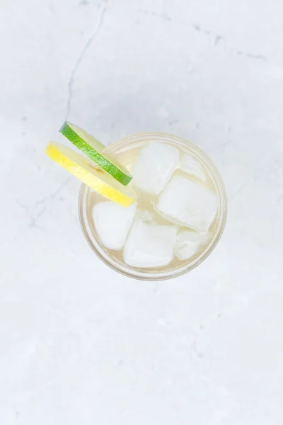 Água com limão e limão em um copo com gelo — Fotografia de Stock
