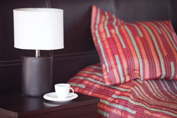 Cama com um travesseiro, uma xícara de chá na mesa de cabeceira e lâmpada — Fotografia de Stock