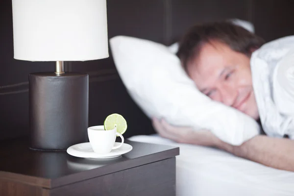 stock image Man sleeping on a bed, a cup of tea on the bedside table and lam