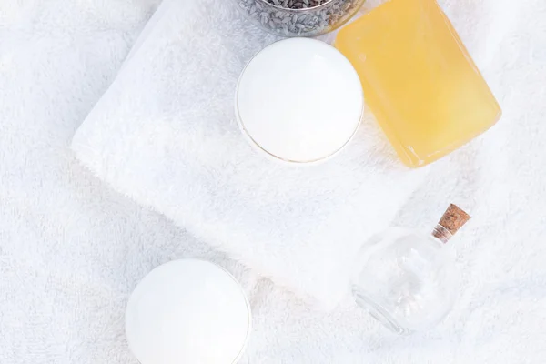 Recipientes cosméticos, botellas, jabón y lavanda sobre una toalla blanca —  Fotos de Stock