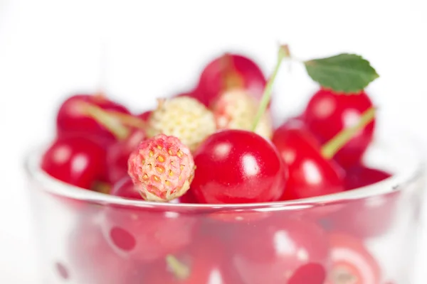Tazza di vetro con ciliegie e fragole selvatiche su uno sfondo bianco — Foto Stock