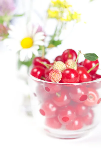 Tazza di vetro con ciliegie e fragole selvatiche e un bouquet di — Foto Stock