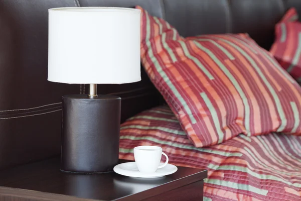 Ágy, egy párna, egy csésze teát, Éjjeliszekrény és lámpa — Stock Fotó
