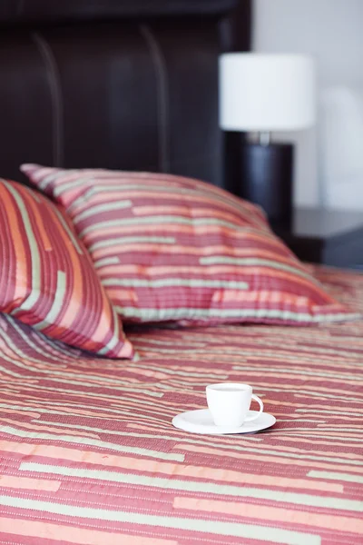 Bed met een kussen, een kopje thee op het nachtkastje en lamp — Stockfoto