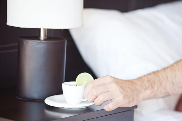 Man hand, een kopje thee op het nachtkastje en lamp — Stockfoto