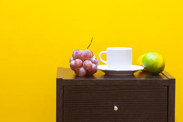 Table de chevet, fruits et tasse contre un mur jaune dans l'appartement — Photo