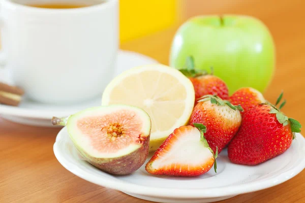 Taza de té, galletas, manzana, limón, higo y fresas en un plato — Foto de Stock