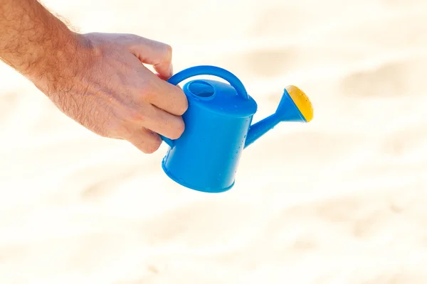 Mão de um homem com uma lata de rega em um fundo de areia — Fotografia de Stock