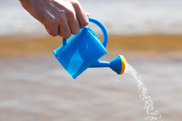 Mão de um homem com uma lata de rega em um fundo de água — Fotografia de Stock