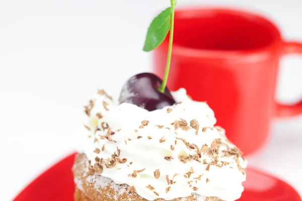 Muffin com chantilly, cerejas e xícara vermelha no backgro branco — Fotografia de Stock