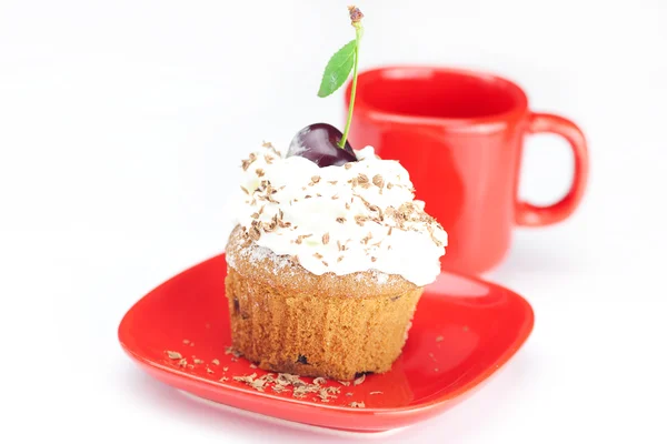 Muffin con crema batida, cerezas y taza roja sobre fondo blanco — Foto de Stock