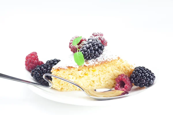 Kake med glasur, skje, bringebær, bjørnebær og mynte på tallerken – stockfoto