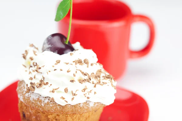 Muffin con crema batida, cerezas y taza roja sobre fondo blanco —  Fotos de Stock