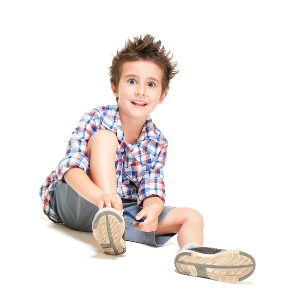 Непослушный волосатый маленький мальчик в шортах и рубашке надевает туфли — стоковое фото