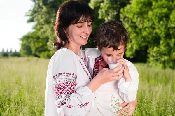 Mère et fils en chemise ukrainienne traditionnelle boivent du lait en plein air — Photo