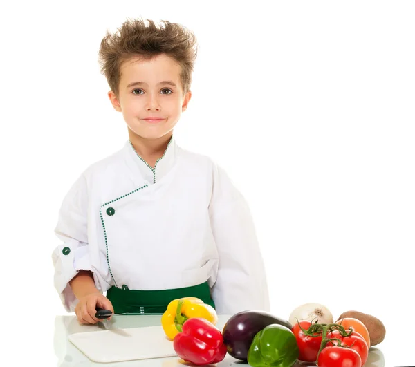 Little boy chef in uniform with knife cutting vegetables — Stock Photo, Image