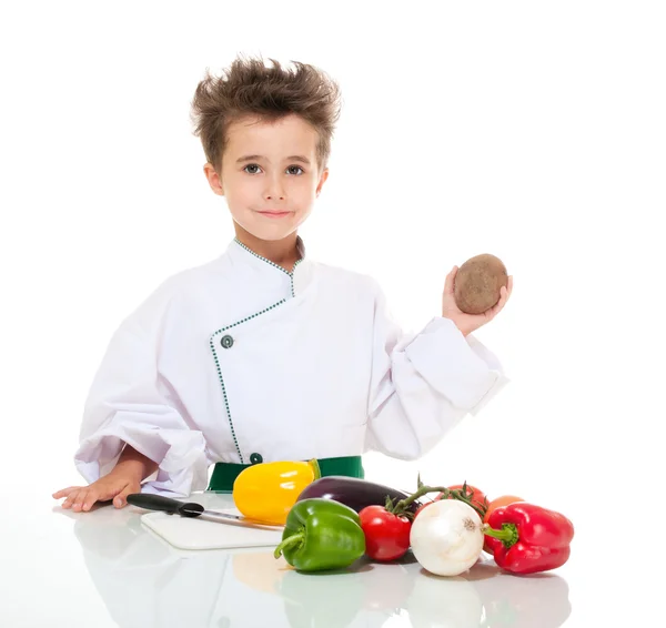 Kleiner Junge kocht in Uniform mit Messer, das Gemüse hält — Stockfoto