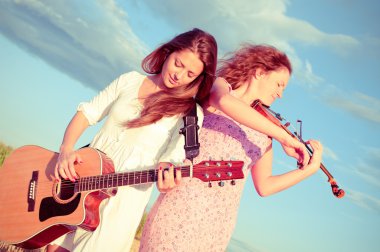 Two young women playing guitar and violin outdoors. Split toning clipart