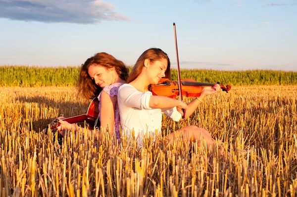Zwei junge Frauen, die draußen Gitarre und Geige spielen — Stockfoto