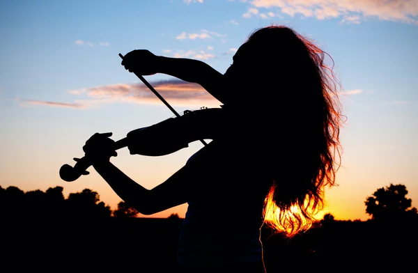 Женский силуэт играет на скрипке в лучах заката — стоковое фото