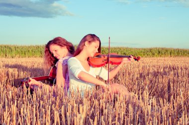 Two young women playing guitar and violin outdoors. Split toning clipart