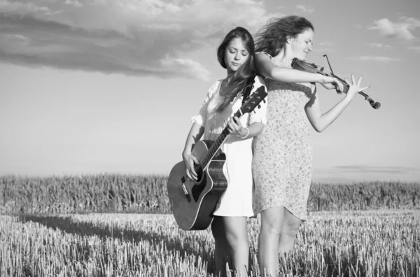 Zwei junge Frauen, die draußen Gitarre und Geige spielen. Graustufen. — Stockfoto