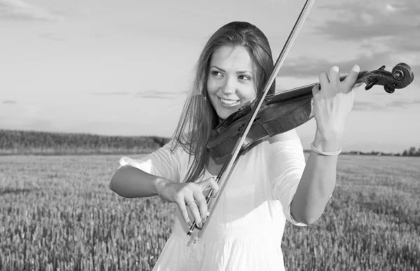 Mujer joven tocando el violín al aire libre en el campo. Escala de grises . — Foto de Stock