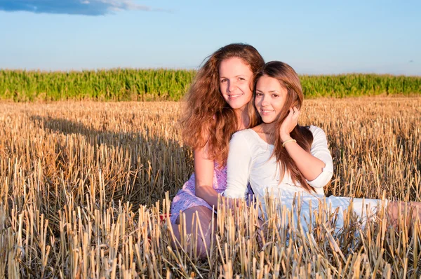 Two girls friends lean each another on summer field — Stock Photo, Image