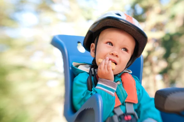 Liten pojke i cykel barnstol äter cracker — Stockfoto