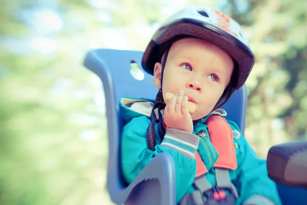 Niño en bicicleta asiento de niño comiendo galleta. Proceso cruzado — Foto de Stock