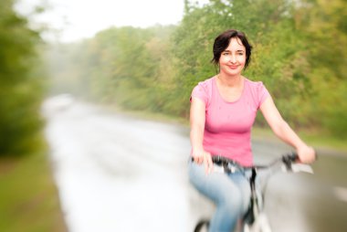 Woman riding bike on the rainy forest road. Lensbaby effect clipart