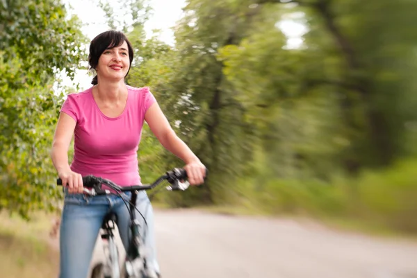 Vrouw rijden fiets op de zomer bos weg. Lensbaby effect — Stockfoto