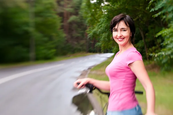 Γυναίκα με ποδήλατο στο δρόμο βροχερό δάσος. Lensbaby επίδραση — Φωτογραφία Αρχείου