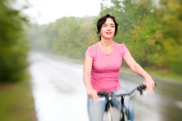 Vrouw met fiets op de regenachtige bos weg. Lensbaby effect — Stockfoto