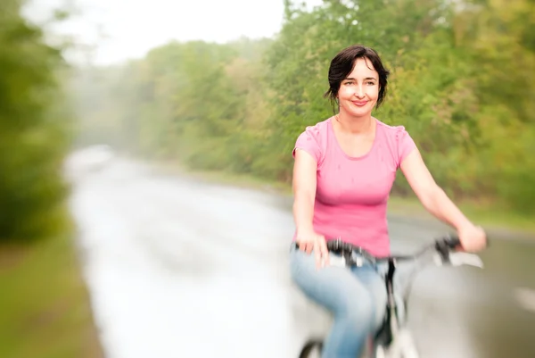 Vrouw rijden fiets op de regenachtige bos weg. Lensbaby effect — Stockfoto