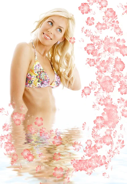 Louro bronzeado em biquíni colorido em pé na água com flores — Fotografia de Stock