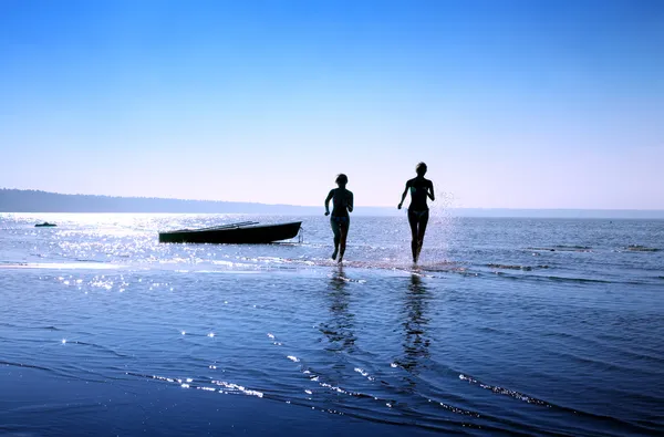 Силуэт изображения двух бегущих девушек в воде — стоковое фото
