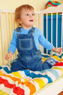 Happy toddler sitting in the baby cot clipart