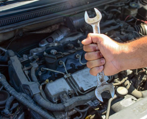 stock image Hand holding spanner against car engine