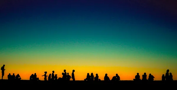 Groupe de jeunes assis sur le mur au coucher du soleil — Photo