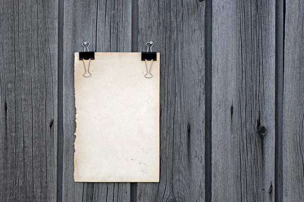 Black clip and old blank note paper hang on wood panel — Stock Photo, Image