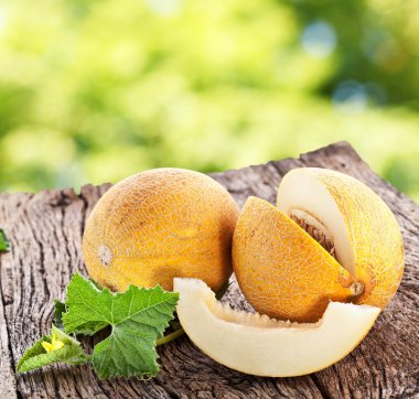 Melon with slices and leaves on a old wooden table. clipart